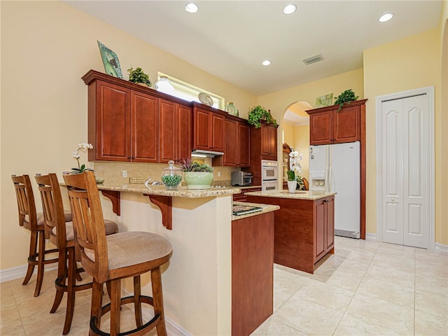 kitchen featuring decorative backsplash, white fridge with ice dispenser, a kitchen island, a breakfast bar, and light stone countertops