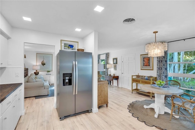 kitchen with stainless steel refrigerator with ice dispenser, a chandelier, pendant lighting, light hardwood / wood-style floors, and white cabinets