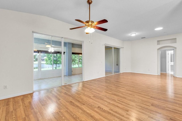 empty room with arched walkways, lofted ceiling, a ceiling fan, wood finished floors, and baseboards