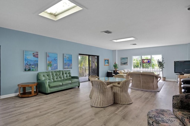 living room featuring a skylight, baseboards, visible vents, and wood finished floors