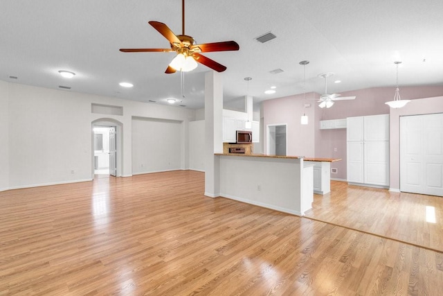 unfurnished living room with visible vents, arched walkways, ceiling fan, vaulted ceiling, and light wood-style floors