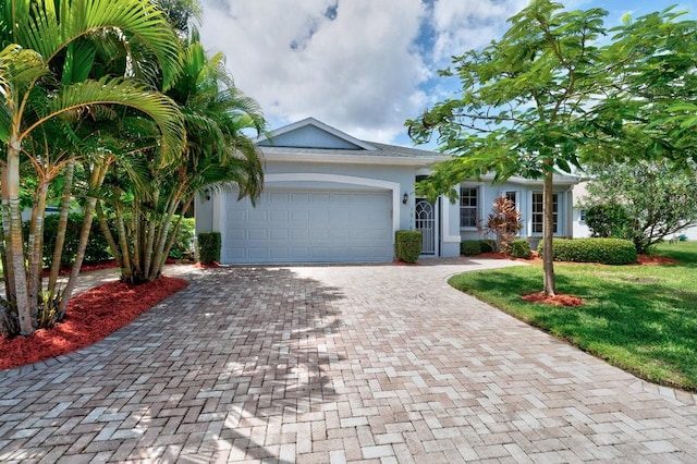 view of front of property featuring a garage, a front yard, decorative driveway, and stucco siding