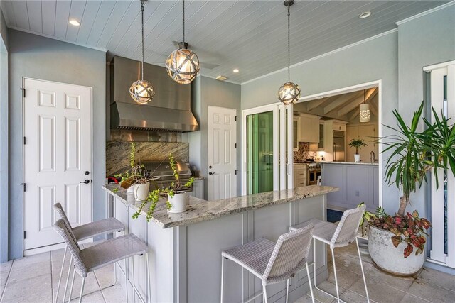 951 W Polo Grounds Dr, Vero Beach, FL 32966 - kitchen with a breakfast bar, light stone countertops, recessed lighting, wall chimney range hood, and crown molding