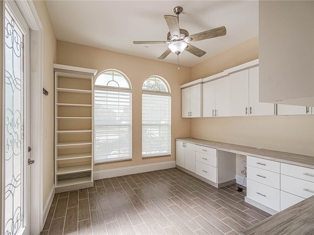 unfurnished office featuring built in desk, ceiling fan, and dark hardwood / wood-style flooring