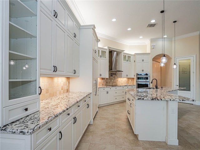 kitchen with a center island with sink, wall chimney exhaust hood, hanging light fixtures, ornamental molding, and double oven