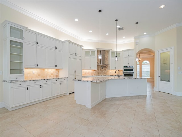 kitchen featuring white cabinetry, a center island with sink, decorative light fixtures, and stainless steel double oven