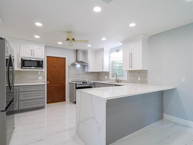 kitchen featuring wall chimney exhaust hood, sink, white cabinetry, kitchen peninsula, and stainless steel appliances