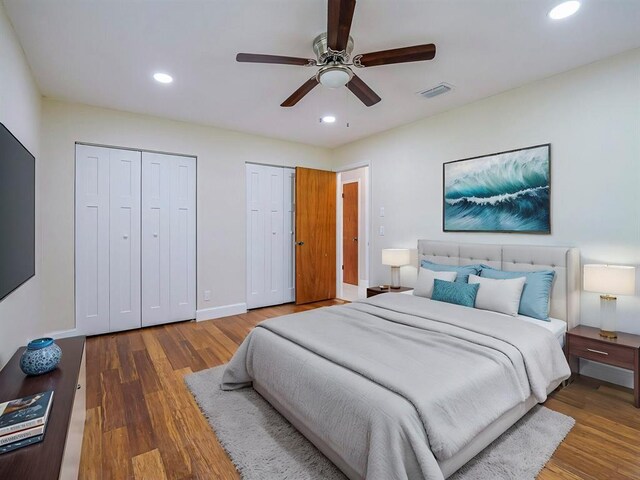 bedroom featuring hardwood / wood-style floors, two closets, and ceiling fan