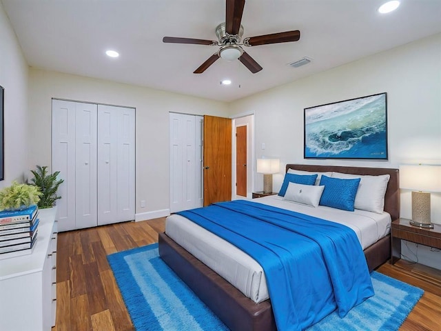 bedroom with ceiling fan, dark wood-type flooring, and multiple closets