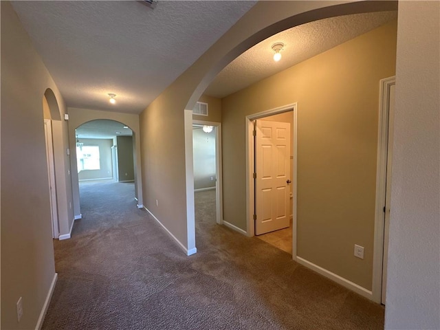 hall with a textured ceiling, visible vents, arched walkways, carpet floors, and baseboards