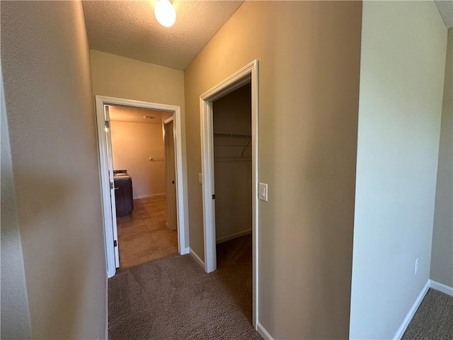 corridor with carpet flooring, a textured ceiling, and baseboards