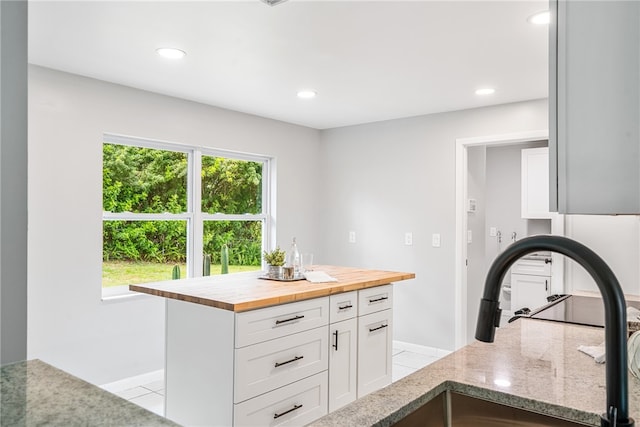 kitchen with light tile patterned flooring, butcher block counters, sink, white cabinets, and a center island