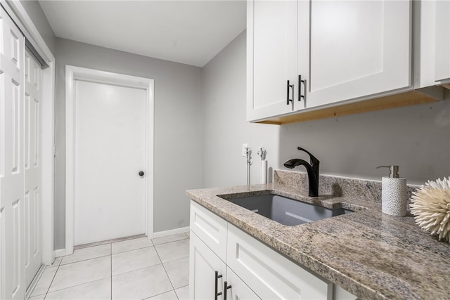 kitchen with light tile patterned flooring, white cabinetry, sink, and light stone countertops