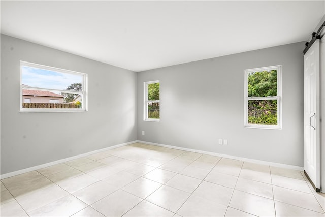 empty room with a barn door, light tile patterned flooring, and plenty of natural light