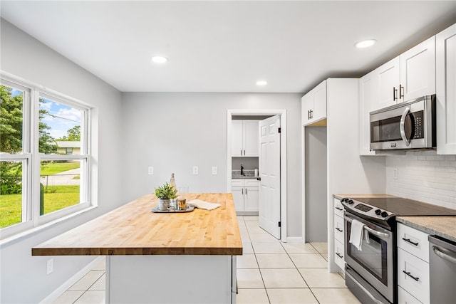 kitchen featuring butcher block counters, white cabinetry, appliances with stainless steel finishes, backsplash, and a center island