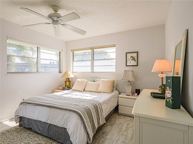 bedroom with a textured ceiling, multiple windows, light hardwood / wood-style floors, and ceiling fan