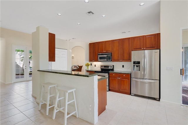 9520 E Maiden Ct, Vero Beach, FL 32963 - kitchen featuring stainless steel appliances, arched walkways, a kitchen bar, dark stone counters, and light tile patterned flooring