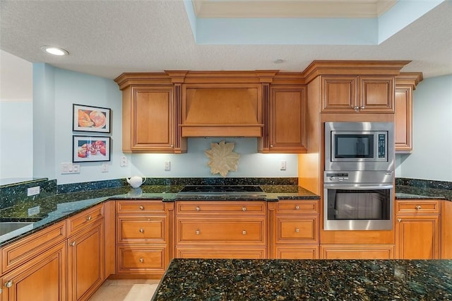 kitchen with stainless steel microwave, dark stone counters, black electric cooktop, custom range hood, and a textured ceiling