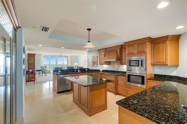 kitchen featuring premium range hood, sink, appliances with stainless steel finishes, a tray ceiling, and kitchen peninsula