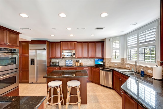 kitchen with stainless steel appliances, dark stone counters, a center island, sink, and light tile patterned flooring