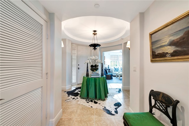 hall featuring light tile patterned flooring, a chandelier, and a tray ceiling