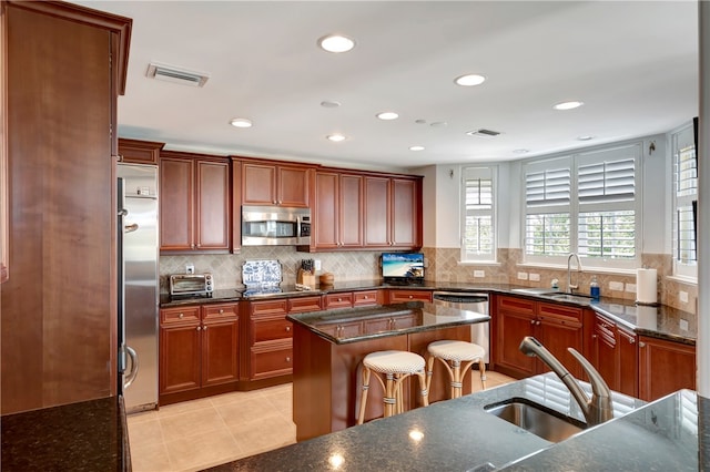 kitchen with stainless steel appliances, a kitchen island, backsplash, sink, and dark stone countertops