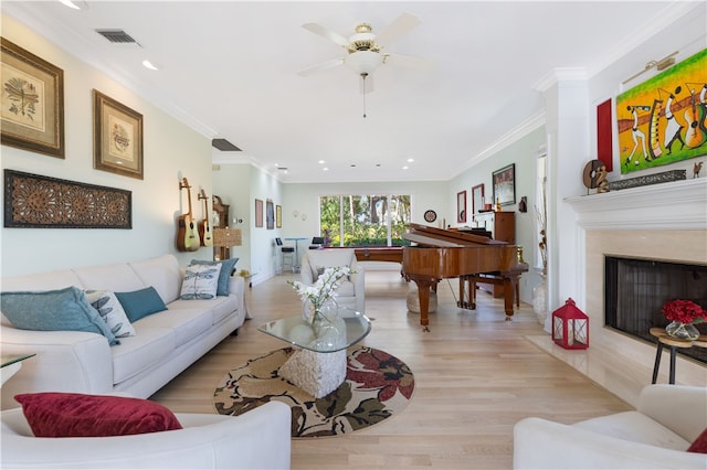 living room with crown molding, light hardwood / wood-style floors, a premium fireplace, and ceiling fan