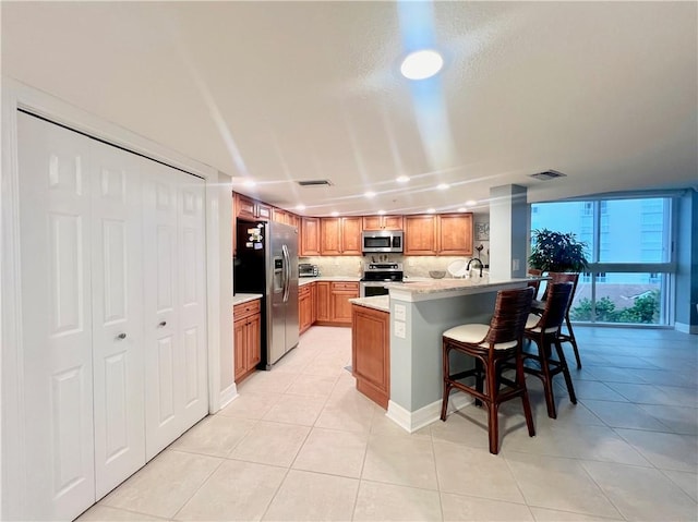 kitchen featuring sink, decorative backsplash, appliances with stainless steel finishes, light tile patterned flooring, and a kitchen bar