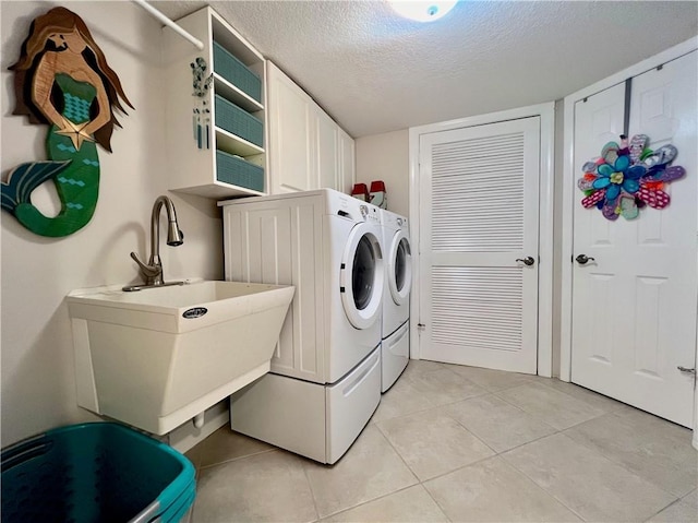 washroom with sink, cabinets, washing machine and dryer, a textured ceiling, and light tile patterned floors