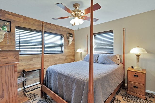 bedroom featuring multiple windows, light hardwood / wood-style flooring, ceiling fan, and wood walls