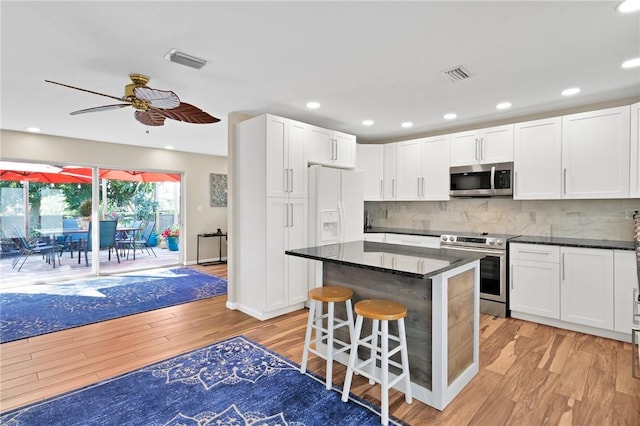 kitchen with white cabinetry, stainless steel appliances, a kitchen bar, and light hardwood / wood-style flooring