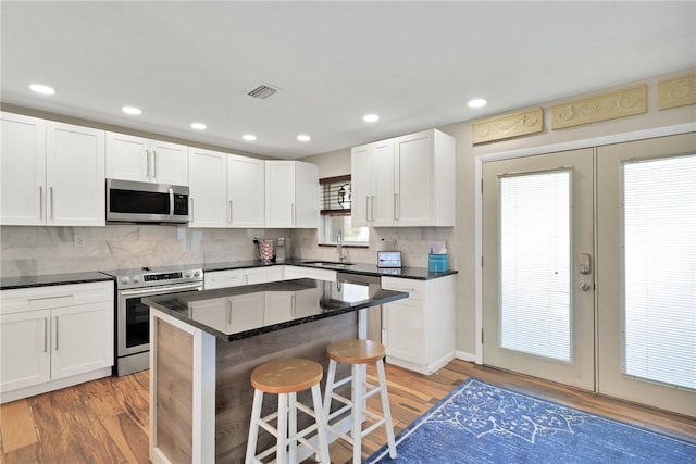 kitchen with stainless steel appliances, a kitchen breakfast bar, a center island, white cabinets, and light wood-type flooring