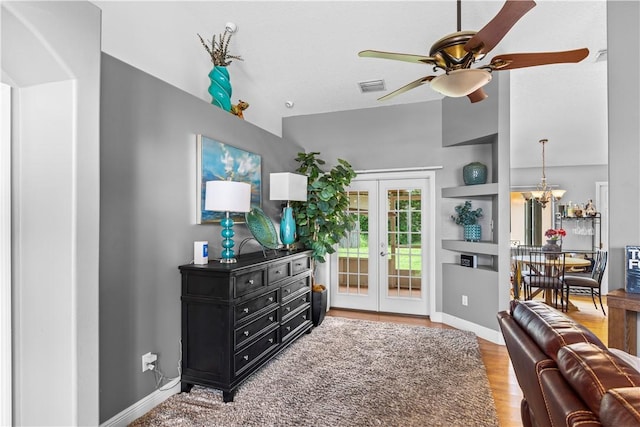 living room featuring visible vents, wood finished floors, baseboards, french doors, and ceiling fan with notable chandelier