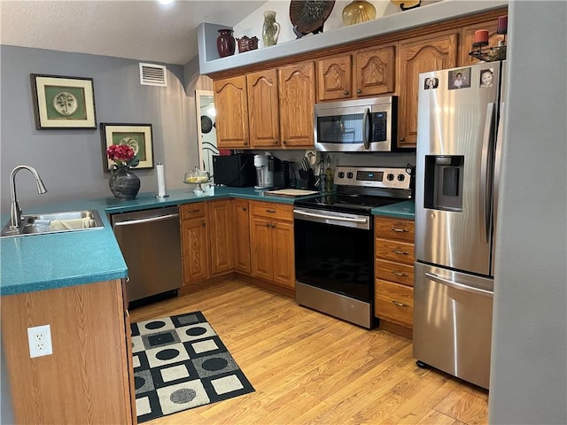 kitchen featuring a sink, light wood-style floors, stainless steel appliances, a peninsula, and visible vents
