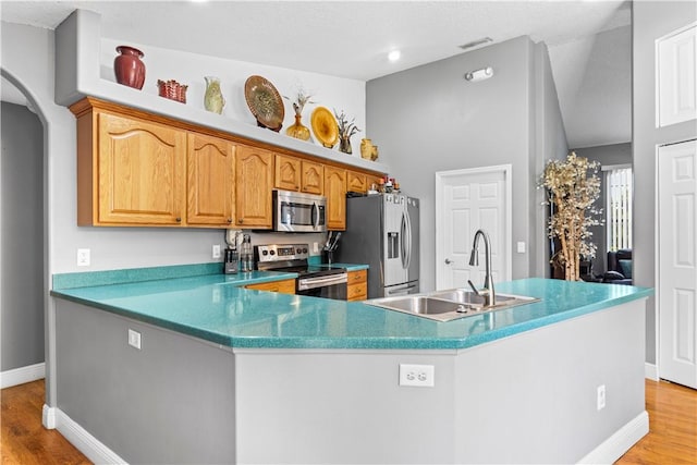 kitchen with baseboards, light wood-type flooring, arched walkways, a sink, and stainless steel appliances