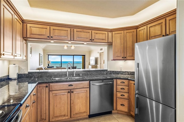 kitchen featuring light tile patterned flooring, brown cabinets, a sink, dark stone countertops, and appliances with stainless steel finishes