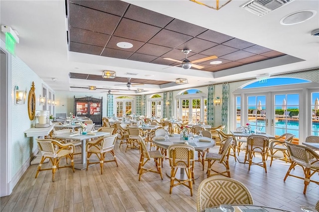 dining space with ceiling fan, a tray ceiling, light wood-style flooring, and visible vents