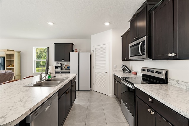 kitchen with a kitchen island with sink, sink, light tile patterned floors, a textured ceiling, and stainless steel appliances