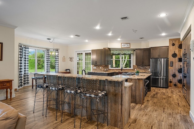 kitchen featuring a kitchen island, a breakfast bar, light wood-type flooring, appliances with stainless steel finishes, and decorative light fixtures