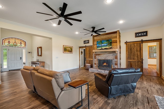 living room with dark wood-type flooring, a barn door, ornamental molding, ceiling fan, and a fireplace