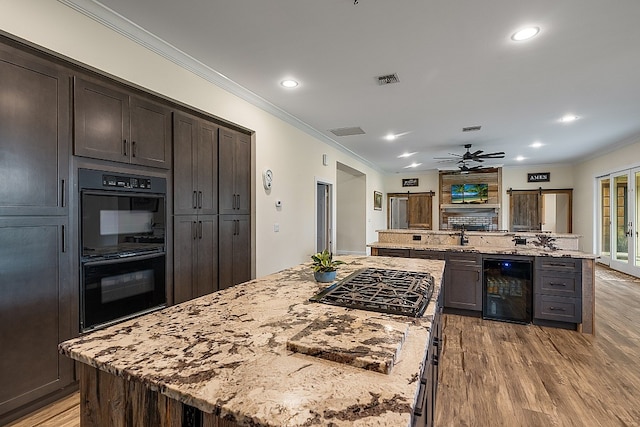 kitchen with light stone countertops, black appliances, wine cooler, and a spacious island