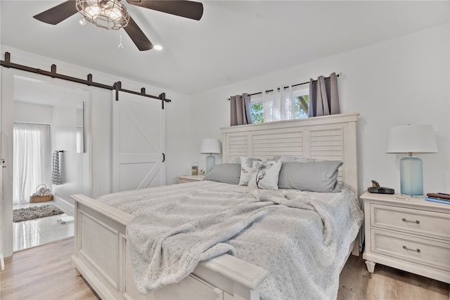 bedroom with ceiling fan, a barn door, and light hardwood / wood-style floors