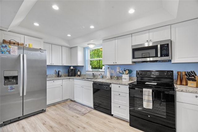 kitchen featuring light hardwood / wood-style flooring, a tray ceiling, white cabinetry, and black appliances