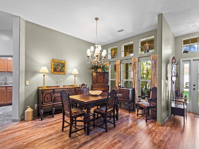 dining space with wood-type flooring, a textured ceiling, sink, and a chandelier