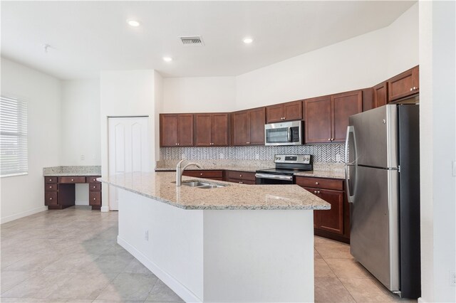 kitchen featuring tasteful backsplash, stainless steel appliances, light stone countertops, sink, and an island with sink