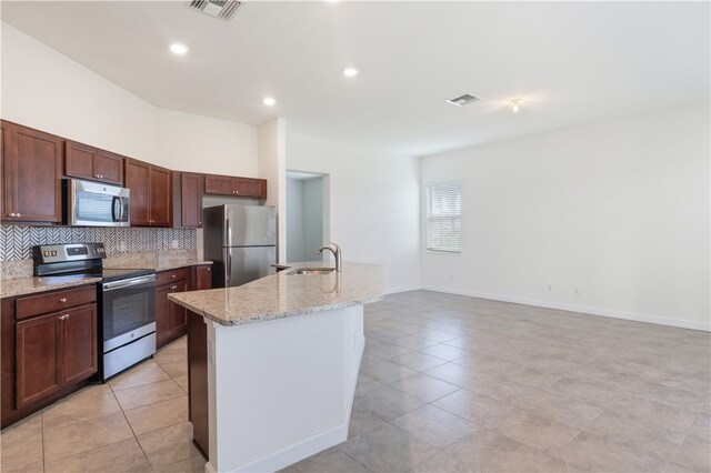 kitchen with stainless steel appliances, a center island with sink, light stone counters, sink, and backsplash