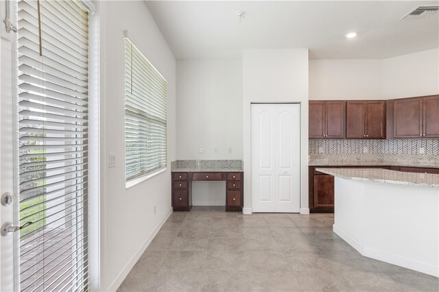 kitchen featuring dark brown cabinetry, decorative backsplash, built in desk, and plenty of natural light