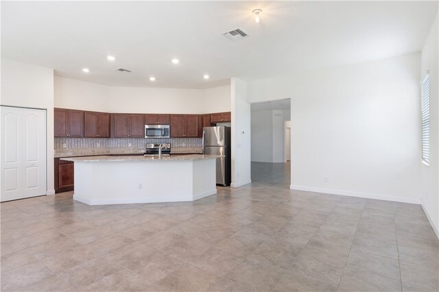 kitchen with a kitchen island with sink, decorative backsplash, stainless steel appliances, and light tile patterned flooring