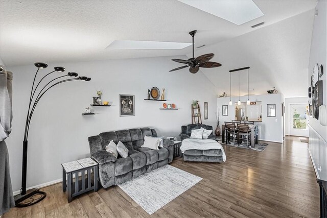 living room with ceiling fan, dark wood-type flooring, and vaulted ceiling with skylight