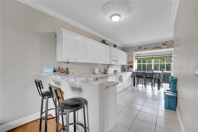 kitchen with kitchen peninsula, a kitchen breakfast bar, white appliances, crown molding, and white cabinets